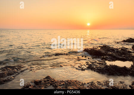 Scharfe Schichten von erodierten Felsen in der reflektierenden Meer und die untergehende Sonne am Horizont auf einem Riff in der Nähe von Paradaisos Strand in Neos Marmaras Stockfoto