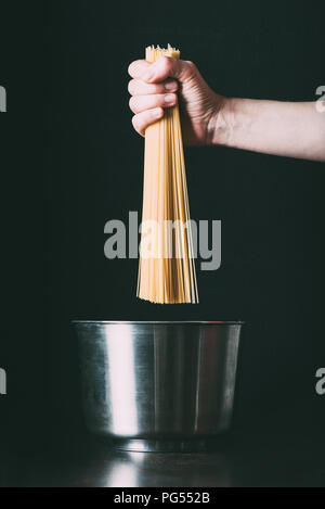 Zugeschnittenes Bild des Menschen die Spaghetti in Pan auf schwarzem Hintergrund Stockfoto