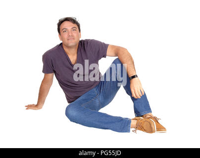 Eine junge schlanke große Mann in Jeans und T-Shirt auf dem Fußboden sitzen entspannt in die Kamera schaut, auf weißem Hintergrund Stockfoto