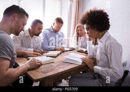 Gruppe von Jungen multiethnischen Menschen Lesen der Bibel über Holz- Schreibtisch Stockfoto