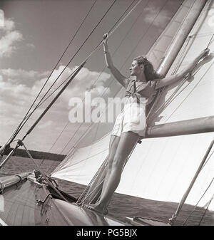 1940 s Segelboot. Eine junge Frau ist an Bord eine modische Segelboot und stehen an Deck und lehnte sich auf den Mast und die Segel, wenn es Kreuzfahrten mit Wind in den Segeln. Sie trägt eine typische 40er Jahre Mode mit einem T-Shirt und Shorts. Schweden 1946 Foto Kristoffersson ref AC 102-5 Stockfoto