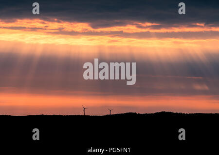 Zwei Windenergieanlagen auf einem Hügel bei Sonnenuntergang in der Nähe von Uddevalla, an der Westküste von Schweden. Sonnenstrahlen (besser bekannt als Sonnenstrahlen bekannt, Sonnenstrahlen. Stockfoto