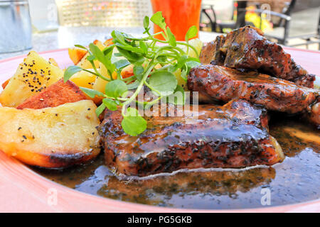 Saftiges Lamm Chunks in dicken Soße mit Bratkartoffeln, garniert mit grünen, serviert in einem pub Garten. Stockfoto