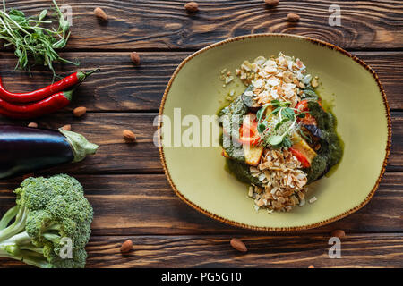 Blick von oben auf die vegetarischen Salat auf Teller und frische Zutaten um auf hölzernen Tischplatte angeordnet Stockfoto