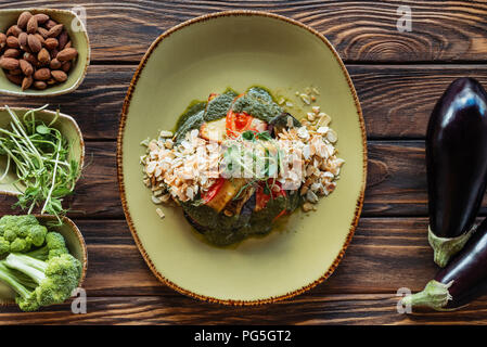 Blick von oben auf die vegetarischen Salat mit geriebenen Mandeln auf dem Teller und frische Zutaten um auf hölzernen Tischplatte angeordnet serviert. Stockfoto