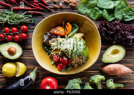 Flach mit vegetarischen Salat mit gegrilltem Gemüse, Sprossen, Kirschtomaten in der Schüssel und arrangierten frischen Zutaten um auf hölzernen Tischplatte Stockfoto