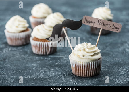 Cremige Cupcakes mit Schnurrbart unterzeichnen und Happy Vatertag Inschrift auf Betonoberfläche Stockfoto