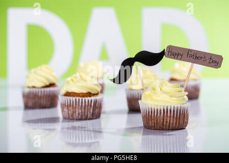 Cremige Cupcakes mit Schnurrbart unterzeichnen und Happy Vatertag Inschrift vor Papa Inschrift aus weißen Buchstaben auf Grün Stockfoto