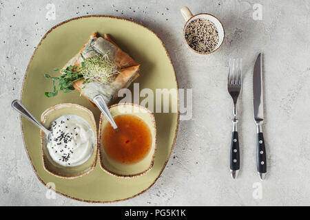 Flach mit Samosas in griescreme Teig mit Spinat und Paneer dekoriert mit gekeimten Samen von Luzerne und Sonnenblumenkerne auf Platte auf Grau gefüllt serviert. Stockfoto