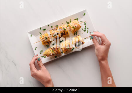 7/8 Bild der Frau, gegrilltem Mais von Platte auf Marmor tisch Stockfoto