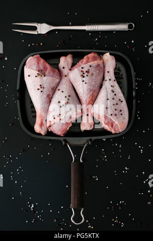Flach mit raw-Türkei Beine mit Pfefferkörner und Salz in Grillpfanne mit Fleisch Gabel auf Schwarz Stockfoto