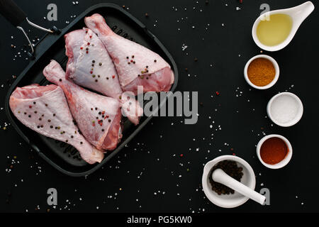 Flach mit der Türkei Beine auf Grillpfanne mit Pfefferkörner, Salz, Öl und Gewürzen auf Schwarzen Tisch Stockfoto