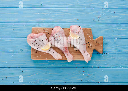 Blick von oben auf die Beine mit rohem Huhn Pfefferkörner und Zitrone auf Holzbrett auf blauen Tabelle Stockfoto