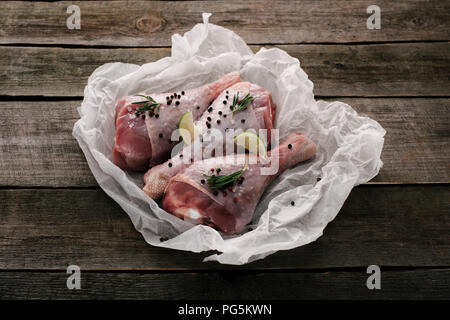 Raw Hähnchenschenkel mit Pfefferkörner und Kalk auf Backpapier auf hölzernen Tischplatte Stockfoto