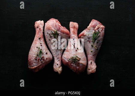 Blick von oben auf die Beine mit rohem Huhn Pfefferkörner und Rosmarin auf schwarze hölzerne Tischplatte Stockfoto