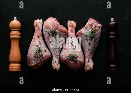 Blick von oben auf die Beine mit rohem Huhn Pfefferkörner und Rosmarin auf hölzernen Tischplatte mit Pfeffer und salzfass Stockfoto