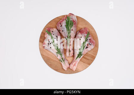 Blick von oben auf die Beine mit rohem Huhn Pfefferkörner und Rosmarin auf Holz Schneidebrett, isoliert auf weißem Stockfoto