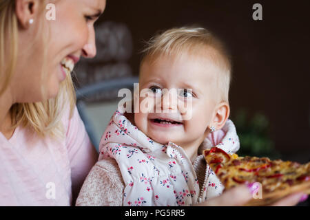 Schöne blonde baby girl in einem wunderschönen weißen Kleid beißen auf Stück leckere Pizza Stockfoto