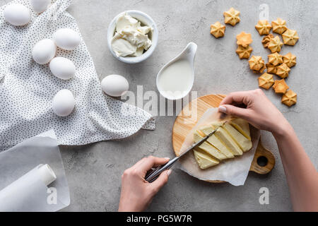 7/8 Schuß von Frau schneiden Butter auf Schneidebrett für hausgemachte Kuchen auf der grauen Tischplatte Stockfoto