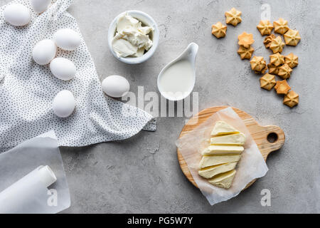 Flach mit geschnittenen Butter, saure Sahne, Cookies und rohem Huhn eier Zutaten für eine Torte auf graue Oberfläche Stockfoto