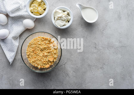 Flach mit zerquetschten Cookies, rohem Huhn Eier und Butter für die Torte auf graue Oberfläche Stockfoto