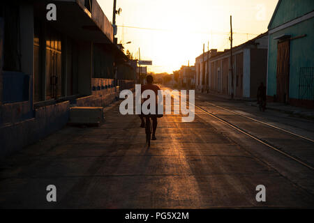 Rückansicht eines kubanischen Menschen Radfahren entlang einer stillgelegten Bahntrasse bis eine Straße in die untergehende Sonne in Cienfuegos Kuba Stockfoto