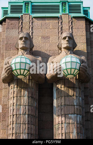 Helsinki Central Railway Station, Blick auf zwei riesige Granitstatuen ('Stone men'), die Globenlichter am Eingang des Bahnhofs in Finnland halten. Stockfoto