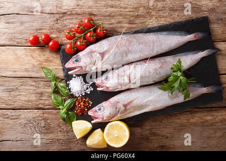 Raw mediterrane Phycis phycis oder gabeldorsch Fisch für das Kochen mit Gewürzen, Gemüse Zutaten close-up auf dem Tisch. horizontal oben Blick von Abo Stockfoto