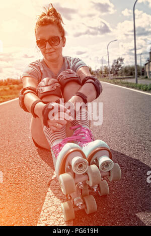 Frau, die in einem Jahrgang Rollschuhe, retro Quad skates Sitzen im Freien. Stockfoto