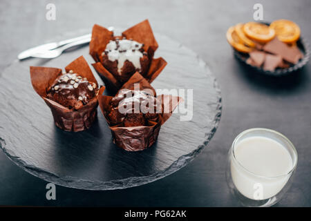 Sweet Muffins mit Schokoladenstückchen und Glas Milch auf schiefer Board Stockfoto