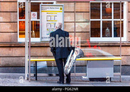 Ein Musiker mit seiner Tuba an einer Bushaltestelle in Newcastle, England, Großbritannien warten Stockfoto