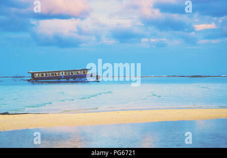 Blick vom Strand auf den Malediven auf der Sandbank und öffentliche Fähre Beförderungsmittels blaue Wasser mit den dramatischen Wolken im Hintergrund. Stockfoto