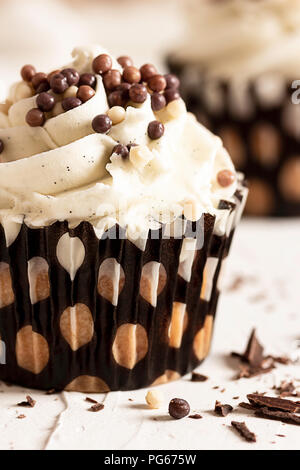 Ein Vanilla Cupcake mit Schokolade Kugeln und einem anderen Cupcake in Soft Focus im Hintergrund gekleidet Stockfoto