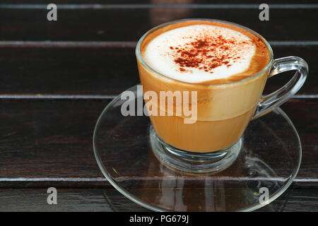 Heißen Cappuccino in transparenten Schale auf dunklen Holztisch serviert. Stockfoto