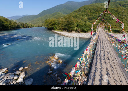 Hölzerne Hängebrücke über eine breite Mountain River an einem sonnigen Tag Stockfoto