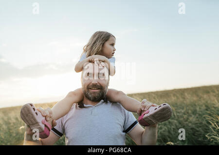 Portrait von lächelnden reifer Mann in der Natur, die kleine Tochter auf seinen Schultern Stockfoto