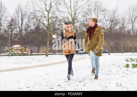 Glückliches junges Paar in Liebe gehen Hand in Hand in einem Park auf verschneiten Tag Stockfoto