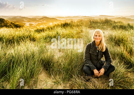 Porträt der lächelnde Frau in den Dünen sitzen Stockfoto