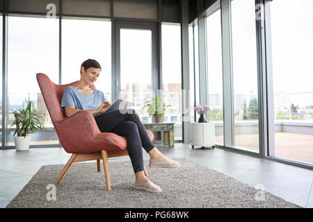 Frau sitzt in einem Sessel mit Tablet home Stockfoto