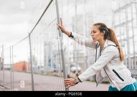 Sportliche junge Frau, die am Bauzaun Stockfoto