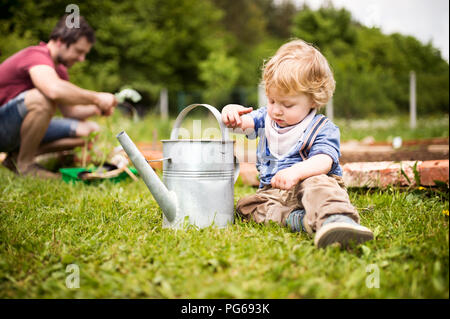 Junge im Garten spielen mit Gießkanne mit Vater im Hintergrund Stockfoto