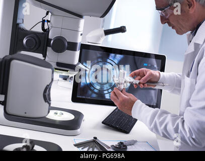 Techniker mit Hilfe einer Schieblehre und ein 3D-Stereo Mikroskop für die Qualitätskontrolle in der Herstellung von technischen Komponenten für die Industrie Stockfoto