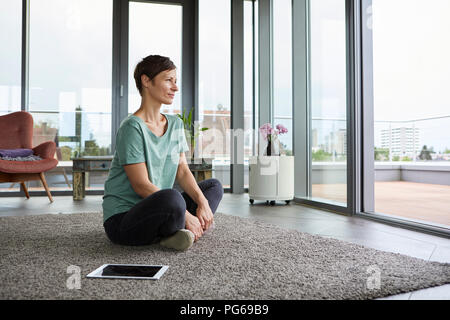 Frau auf dem Boden sitzend zu Hause mit Tablet aus Balkon Tür Stockfoto