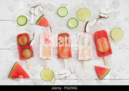 Hausgemachte Wassermelone und Kokosmilch Eis am Stiel mit Kalk und Gurkenscheiben, frische Kokosnuss Chips auf Eiswürfel Stockfoto