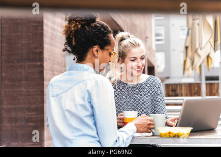 Junge Kolleginnen und Kollegen draußen sitzen, zusammen arbeiten, mit Mittagessen Stockfoto