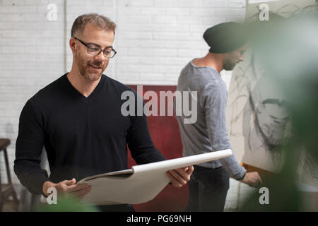 Lächelnd Mann an Skizzenbuch in Artist's Studio suchen Stockfoto