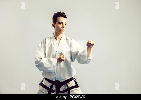 Mädchen im Karate Anzug kimono im Studio am grauen Hintergrund. Weibliches Kind zeigt, Judo oder Karate stans in weiße Uniform mit schwarzem Gürtel. Einzelnen martial Stockfoto