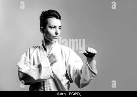 Mädchen im Karate Anzug kimono im Studio am grauen Hintergrund. Weibliches Kind zeigt, Judo oder Karate stans in weiße Uniform mit schwarzem Gürtel. Einzelnen martial Stockfoto