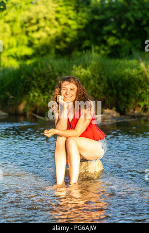 Junge Frau sitzt auf Stein, Fluss Stockfoto