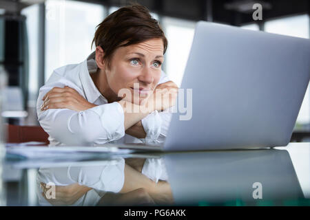 Geschäftsfrau, lehnend auf Glastisch im Amt auf Laptop Stockfoto